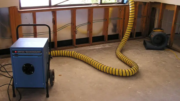 Dehumidifier and air mover with a yellow duct drying an open wall cavity
