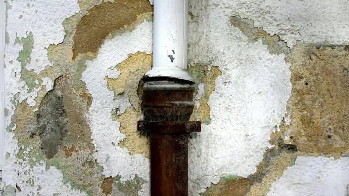 Rusted drain pipe with peeling, water-stained plaster on a wall