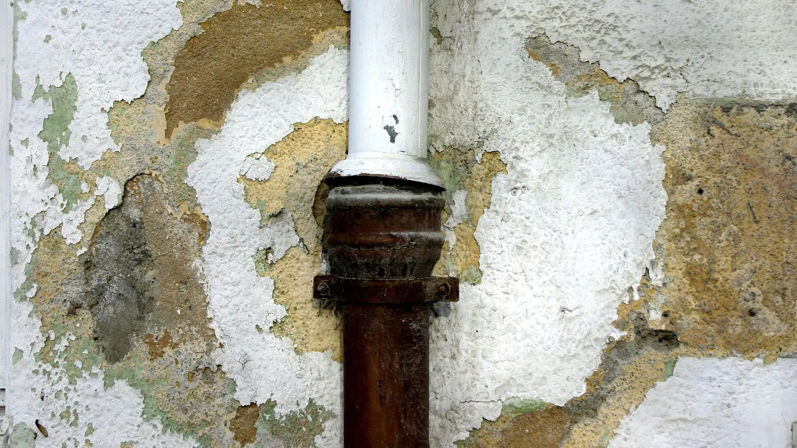 Rusted drain pipe with peeling, water-stained plaster on a wall