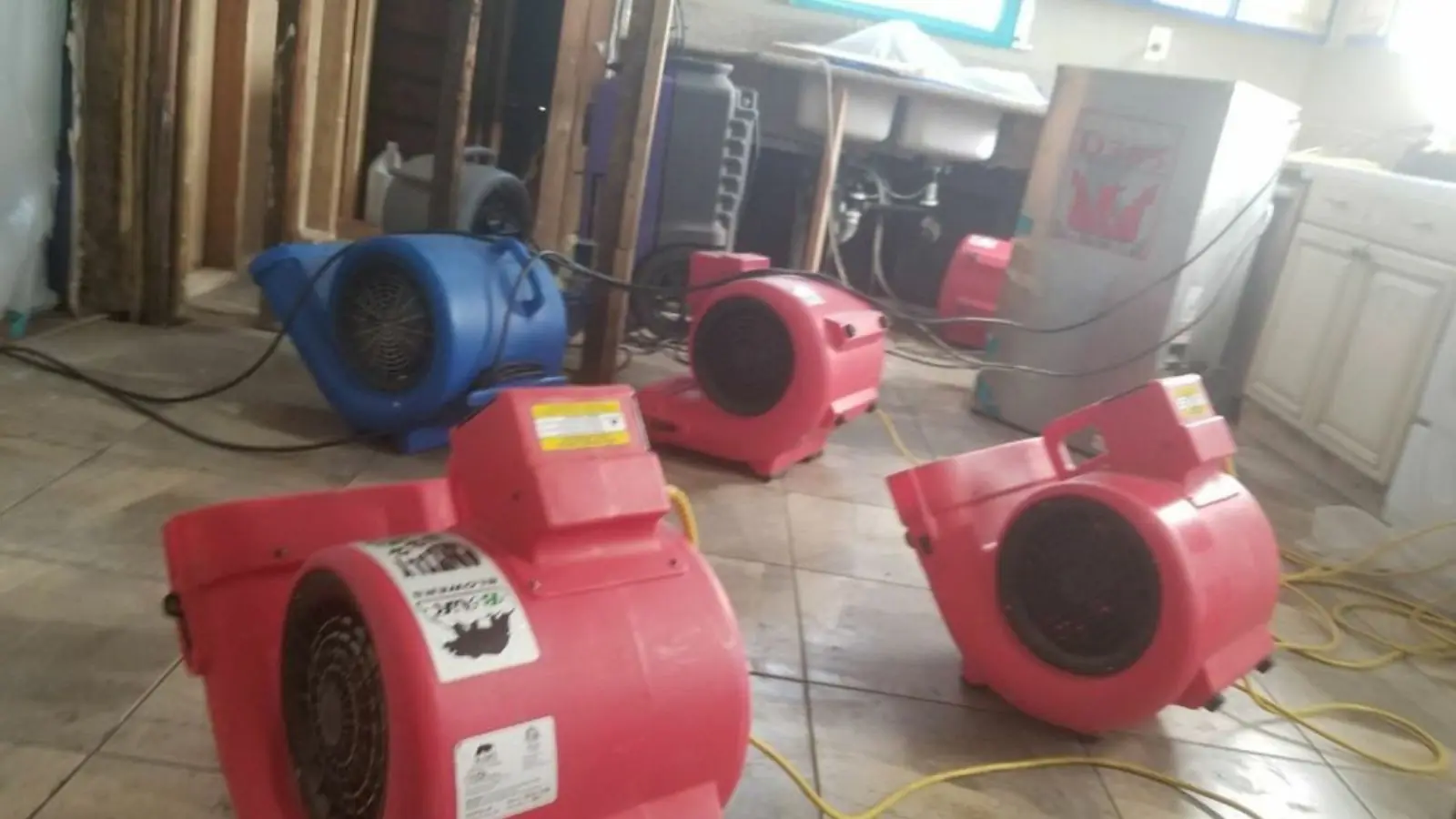 Red air movers drying a room with the lower wall cut open